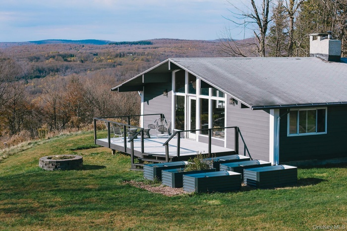 View of side of property with an outdoor fire pit, a deck with mountain view, a view of trees, a chimney, and a yard