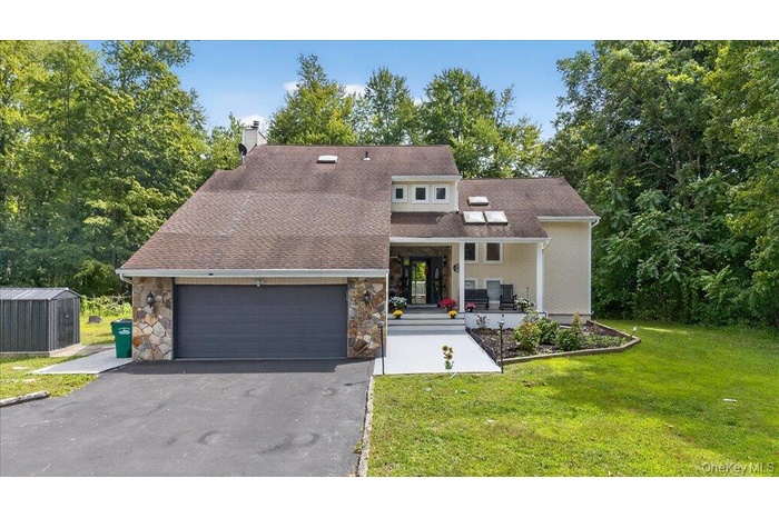 View of front of property featuring a chimney, a porch, a front yard, driveway, and stone siding