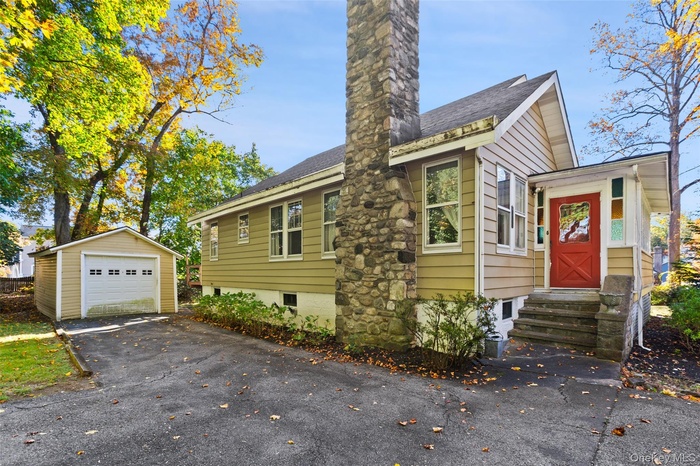 View of front facade with a garage, an outdoor structure, a chimney, and a shingled roof