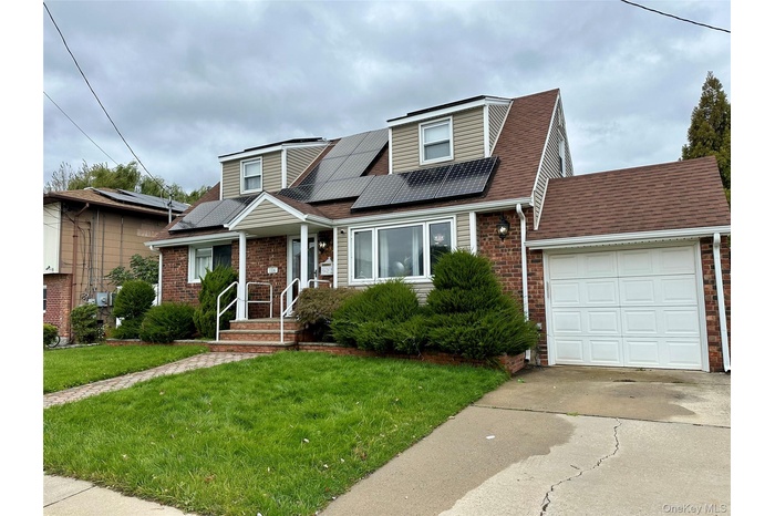 View of front facade featuring solar panels, a front lawn, an attached garage, driveway, and a shingled roof