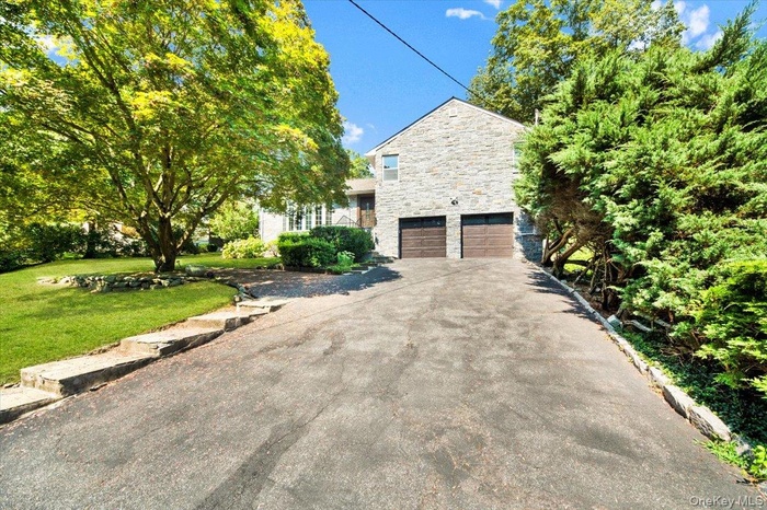 View of front of property with stone siding, an attached garage, asphalt driveway, and a front lawn