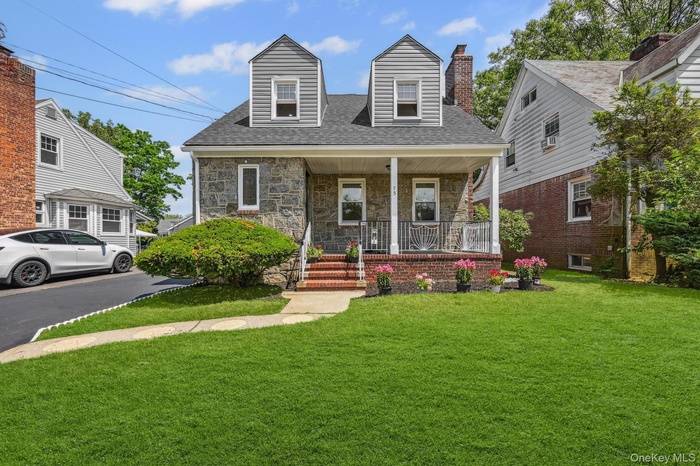 View of front of house featuring covered porch, stone siding, a front lawn, and a shingled roof