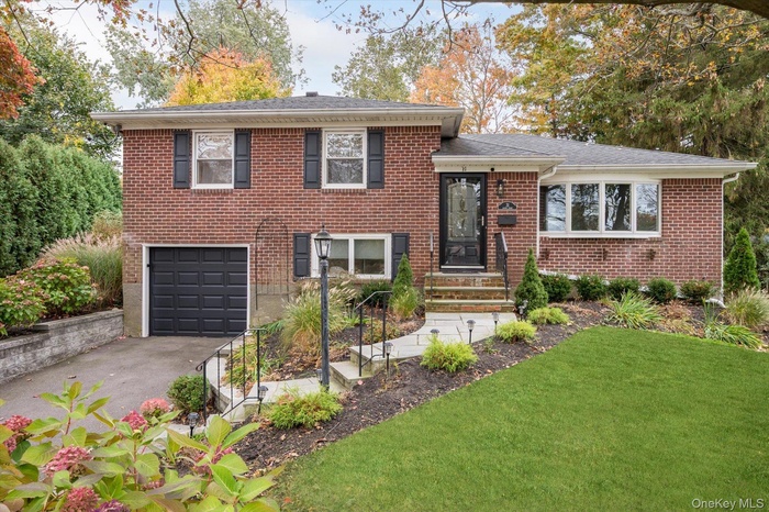 Split level home featuring brick siding, a garage, asphalt driveway, and a front lawn