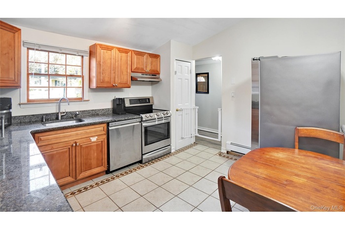 Kitchen with light tile patterned floors, brown cabinets, dark stone countertops, appliances with stainless steel finishes, and vaulted ceiling