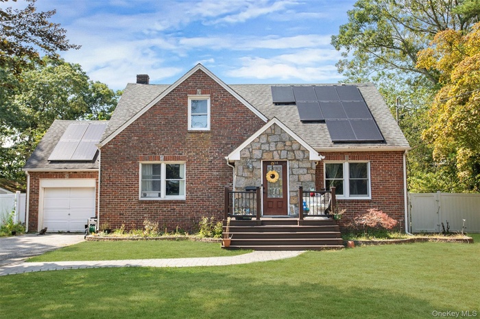 Tudor-style house with roof mounted solar panels, brick siding, driveway, a gate, and a garage