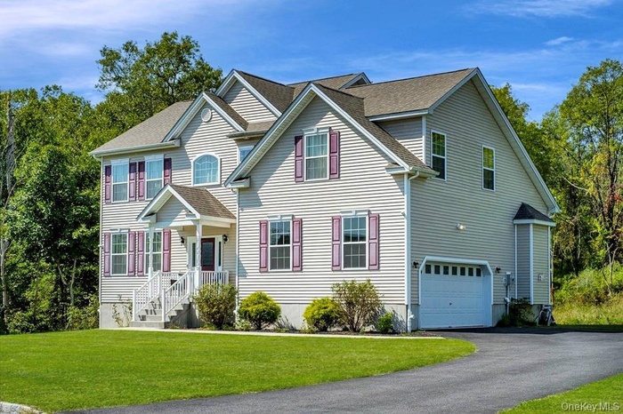 View of front of property featuring a garage, asphalt driveway, roof with shingles, and a front lawn