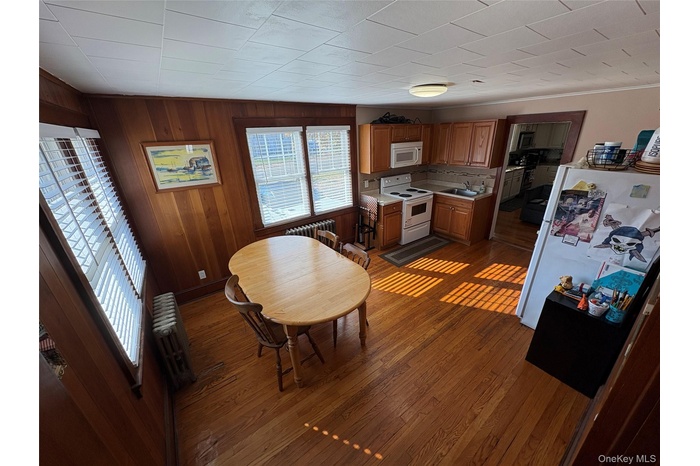 Kitchen with white appliances, wooden walls, brown cabinets, dark wood-type flooring, and light countertops