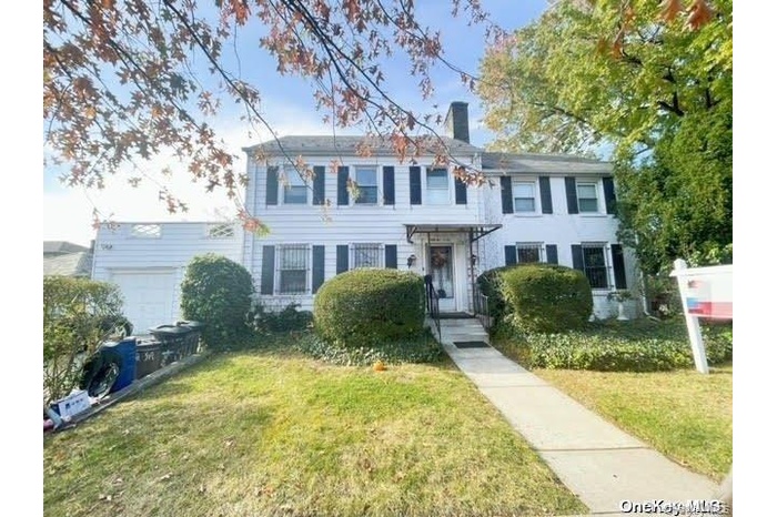 Colonial house featuring a garage, a front yard, cooling unit, and a chimney