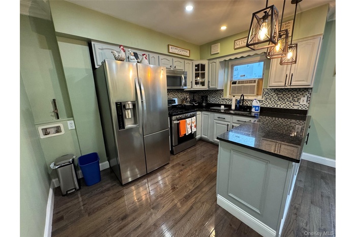 Kitchen featuring stainless steel appliances, dark wood-type flooring, glass insert cabinets, tasteful backsplash, and pendant lighting