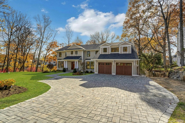 Shingle-style home featuring decorative driveway, covered porch, a front yard, a shingled roof, and a garage