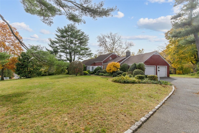 View of front facade featuring a front yard, a chimney, driveway, and a garage