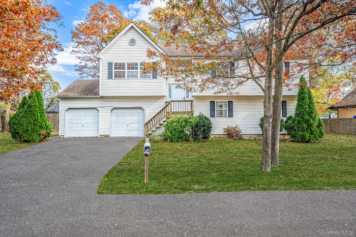 Raised ranch featuring driveway, an attached garage, and roof with shingles