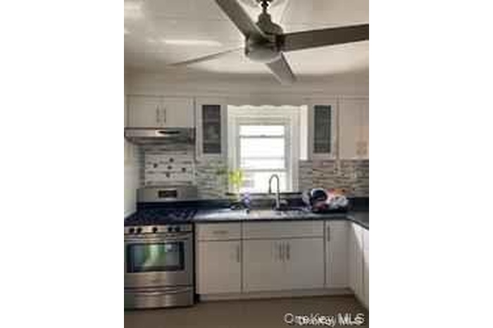 Kitchen with stainless steel gas range oven, glass insert cabinets, dark countertops, white cabinetry, and backsplash