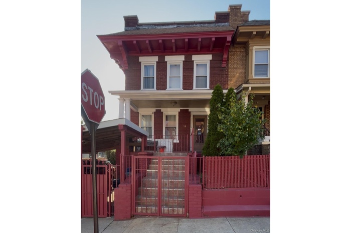 View of front of home with brick siding, a gate, a fenced front yard, and a porch