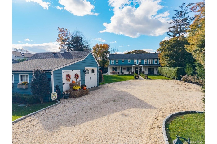 View of front of home featuring dirt driveway, a garage, a shingled roof, a front lawn, and a porch