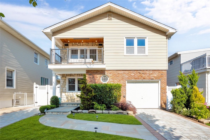 View of front of home featuring a balcony, a gate, decorative driveway, an attached garage, and brick siding