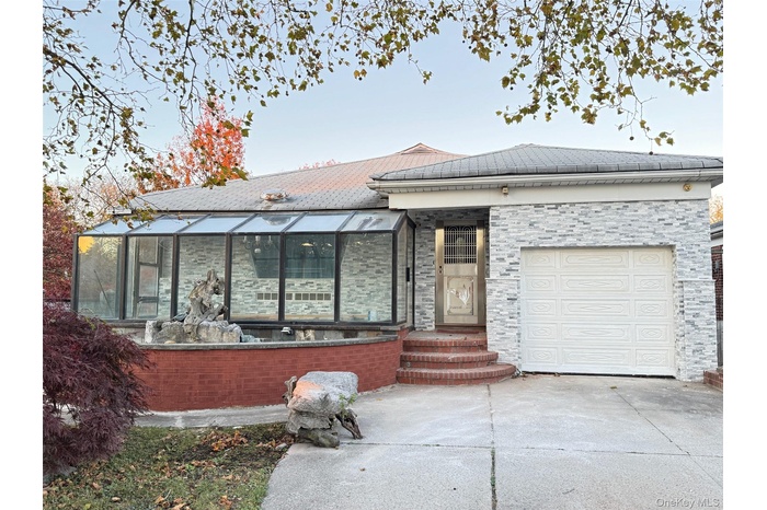 View of front facade with a garage, concrete driveway, and a sunroom