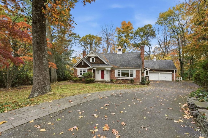 View of front facade featuring a chimney, driveway, a front lawn, brick siding, and a garage
