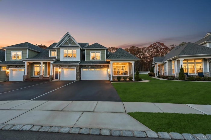 View of front facade featuring driveway, stone siding, a front yard, and an attached garage