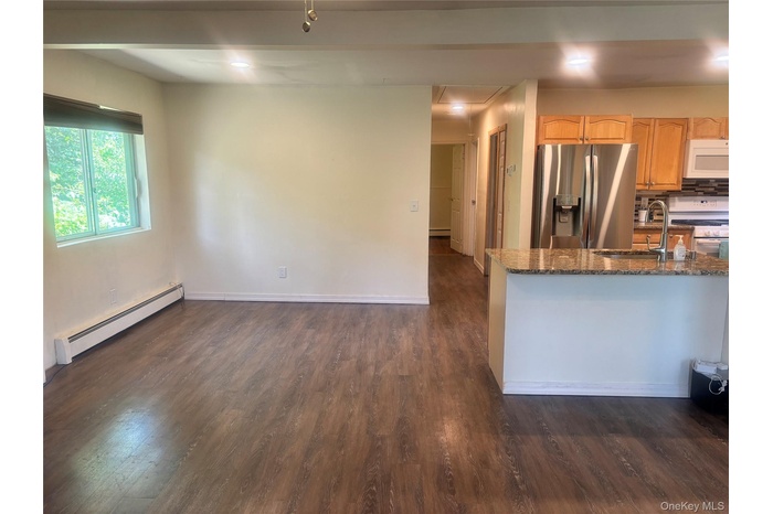 Kitchen with a baseboard heating unit, white appliances, dark wood finished floors, dark stone counters, and backsplash