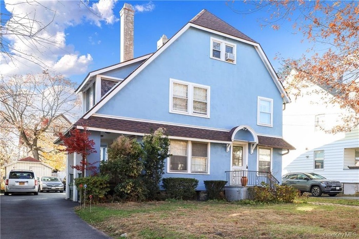 View of front of home with stucco siding, a shingled roof, a chimney, and a front lawn