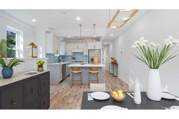 Kitchen featuring decorative backsplash, white cabinetry, light wood-style floors, stainless steel appliances, and hanging light fixtures
