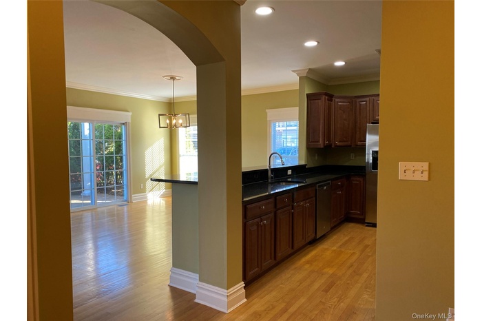 Kitchen with ornamental molding, hanging light fixtures, light wood-type flooring, dark stone countertops, and arched walkways