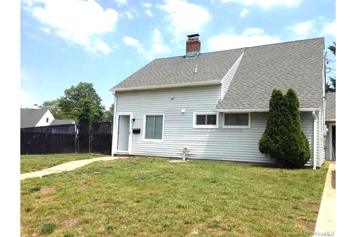 Back of house with a chimney and roof with shingles