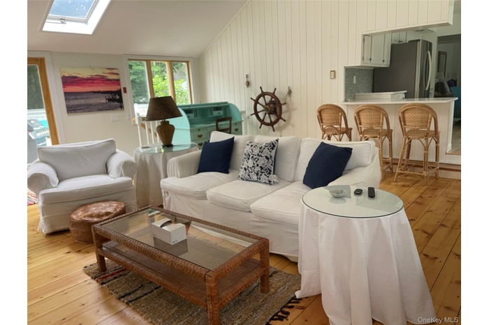 Living room with light wood-type flooring, lofted ceiling, a skylight, and wood walls