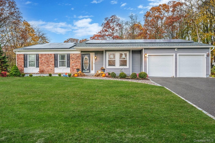 View of front of home with a front lawn, driveway, solar panels, an attached garage, and brick siding