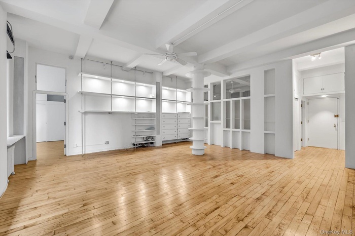 Unfurnished living room featuring light wood finished floors, a ceiling fan, and beam ceiling