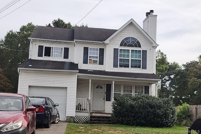 Traditional-style house featuring covered porch, a chimney, an attached garage, and a shingled roof