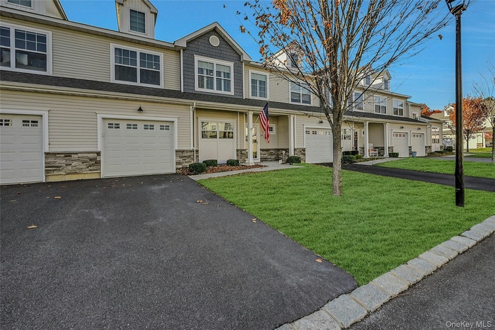 View of front of home with stone siding, a front yard, driveway, a residential view, and a garage
