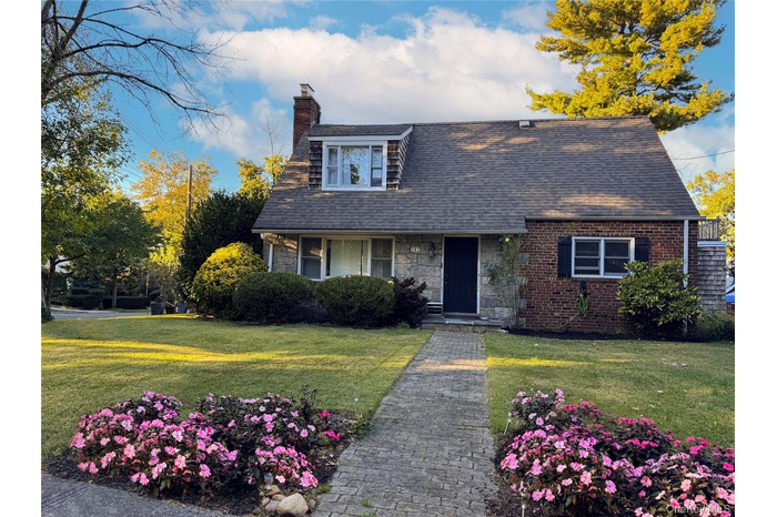 View of front of house with a chimney, a front lawn, roof with shingles, and brick/stone siding