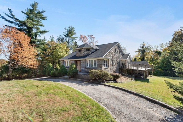 Shingle-style home with a front yard, stone siding, and a deck