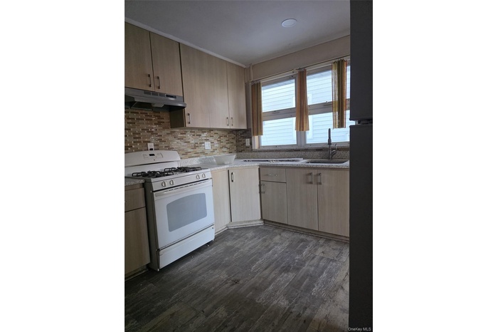 Kitchen with gas range gas stove, light brown cabinetry, dark wood-style floors, under cabinet range hood, and backsplash
