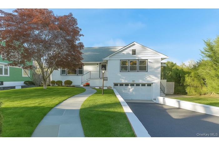 View of front of house featuring a front yard, a garage, a shingled roof, and driveway
