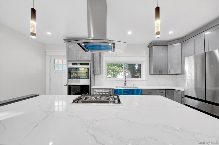 Kitchen with island exhaust hood, healthy amount of natural light, pendant lighting, stainless steel appliances, and recessed lighting