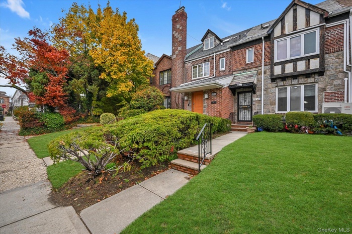 View of front of house featuring a chimney, a front lawn, brick siding, stone siding, and a high end roof
