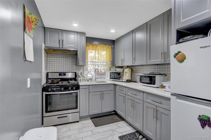 Kitchen featuring white appliances, gray cabinets, decorative backsplash, under cabinet range hood, and recessed lighting