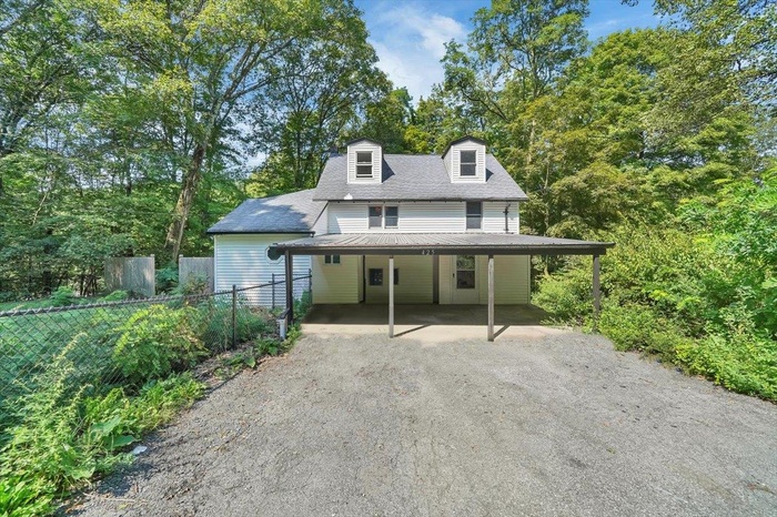 View of front of home with dirt driveway, a carport, a metal roof, and roof with shingles