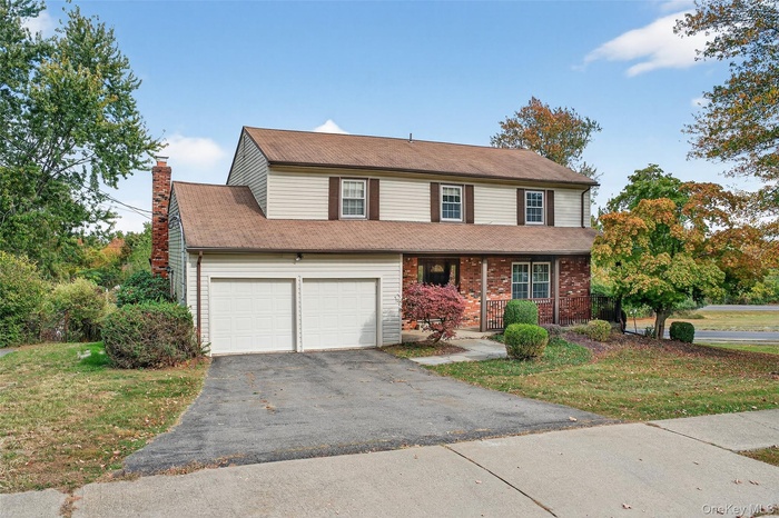 Traditional-style home with a front yard, a chimney, a garage, asphalt driveway, and covered porch