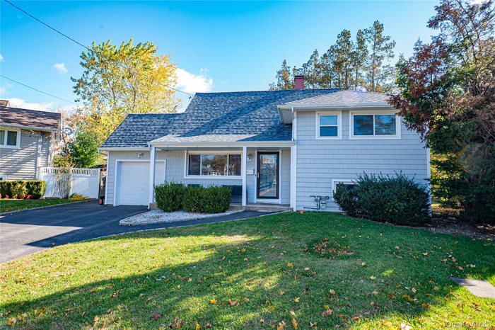 Split level home featuring a shingled roof, asphalt driveway, a chimney, and an attached garage