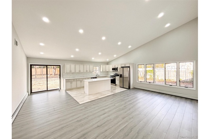 Kitchen with open floor plan to living room, appliances with stainless steel finishes, white cabinets, and baseboard heating