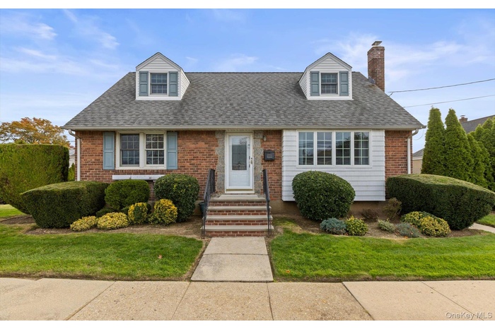 Cape cod-style house with roof with shingles, a chimney, a front lawn, and brick siding
