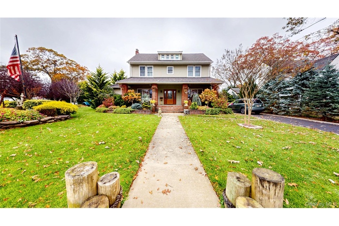 American foursquare style home with covered porch, a chimney, a front yard, and a shingled roof