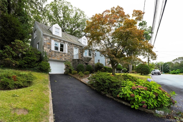 Cape cod house featuring stone siding, an attached garage, and driveway