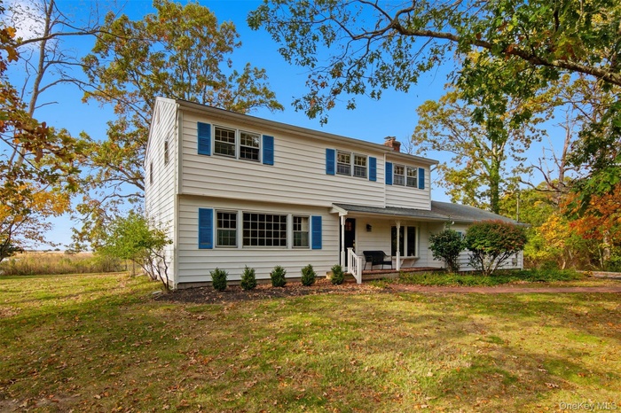 Colonial house featuring a front lawn, a chimney, and a porch
