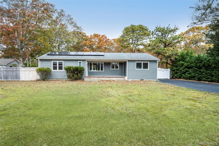 Ranch-style home with roof mounted solar panels, a shingled roof, and view of scattered trees