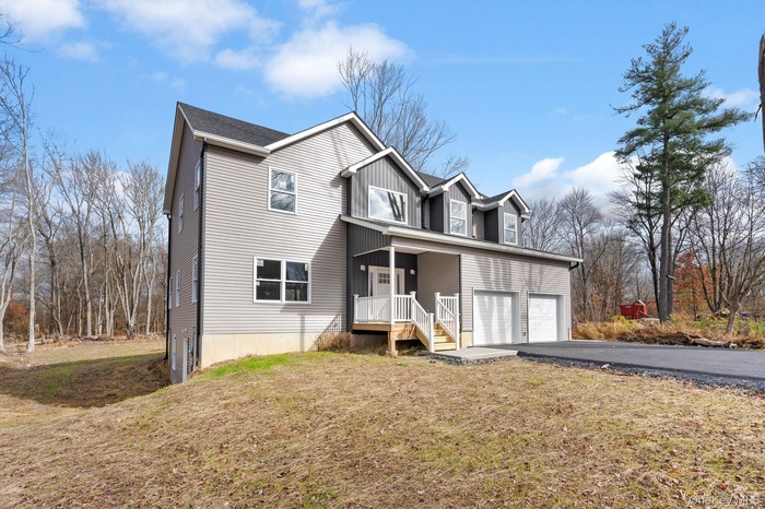 Traditional-style house with a front lawn, asphalt driveway, an attached garage, covered porch, and board and batten siding